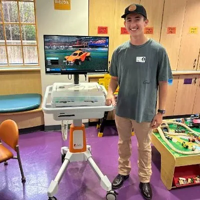 Smithers standing next to a Gamers Outreach GO Kart gaming cart in a hospital playroom